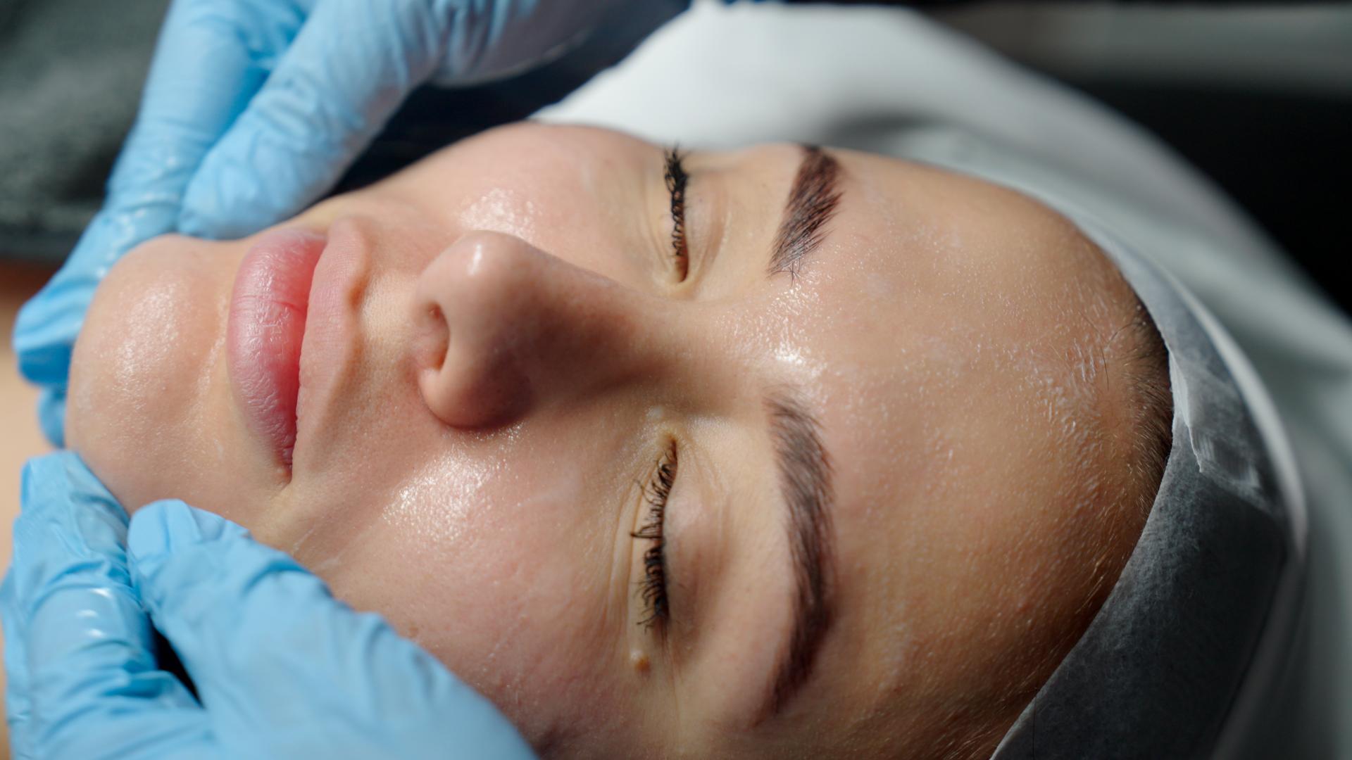 Gloved hands resting gently on a client’s face during a facial.