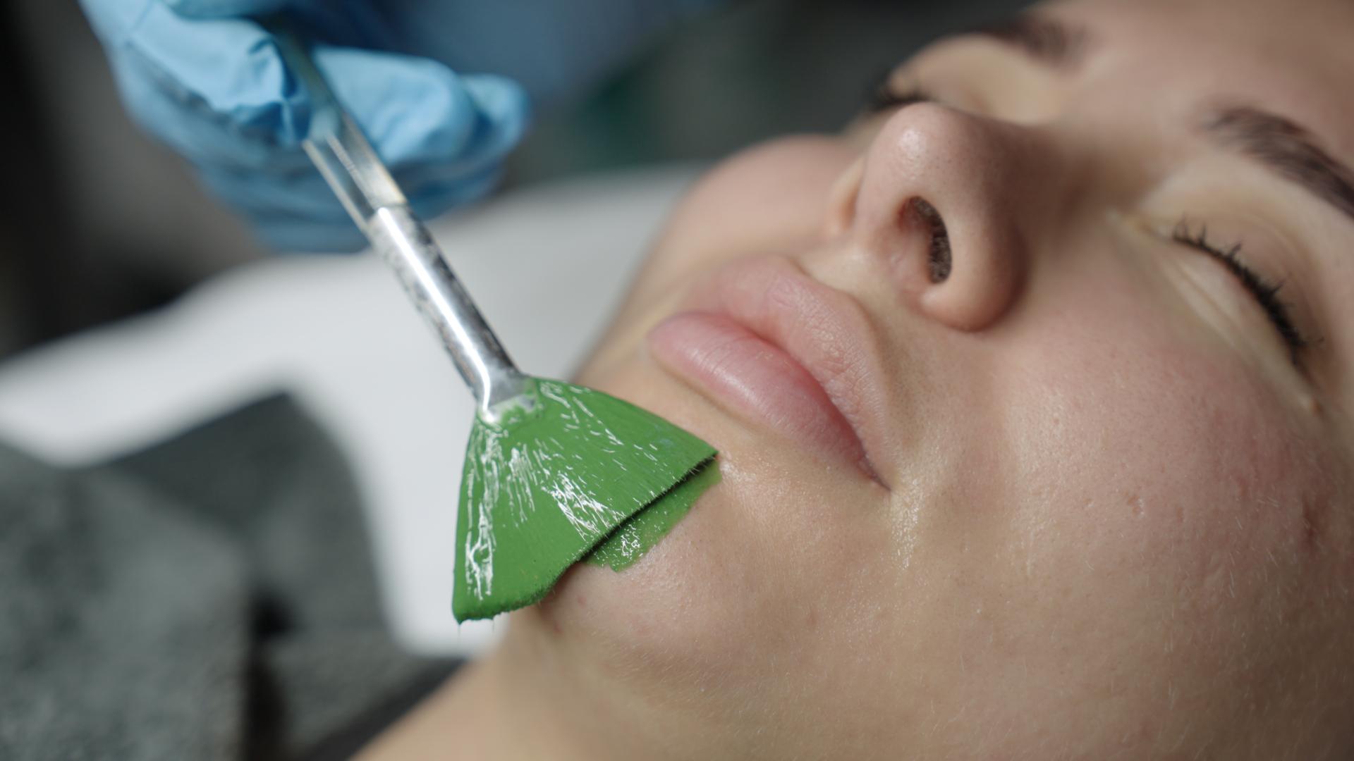A green mask being brushed onto a client’s face.