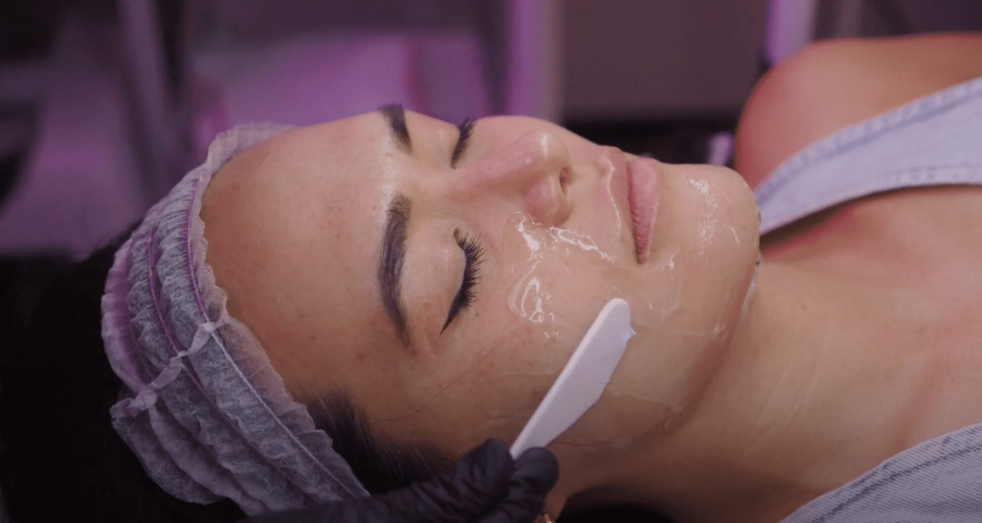 A clear gel mask being applied to a client’s cheek with a spatula.